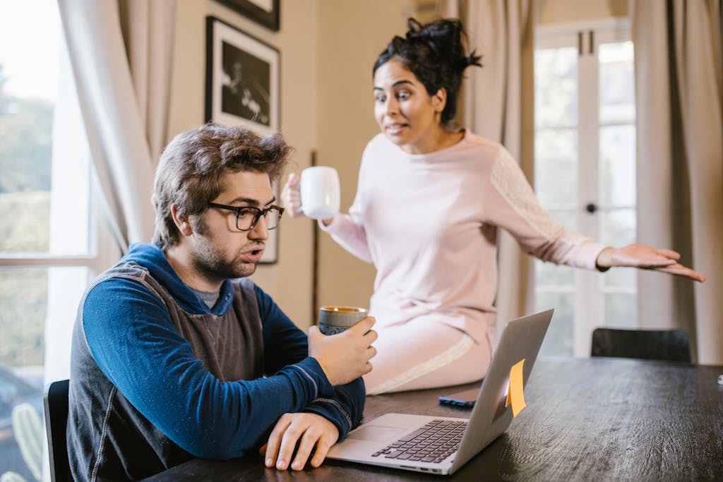 A Man Sitting in Front of a Laptop Beside an Upset Woman